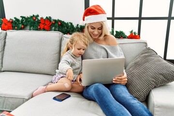 Mother and daughter using laptop sitting by christmas decor at home