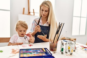 Mother and daughter smiling confident painting palm hands at art studio