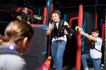 Fototapeta na wymiar Laughing players young mens and womens playing in teams in dark laser tag station