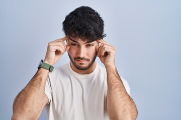 Hispanic man with beard standing over white background trying to open eyes with fingers, sleepy and tired for morning fatigue