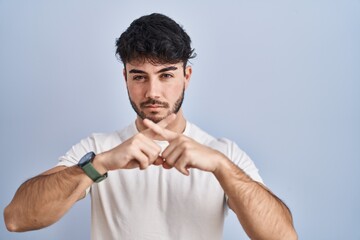 Hispanic man with beard standing over white background rejection expression crossing fingers doing negative sign