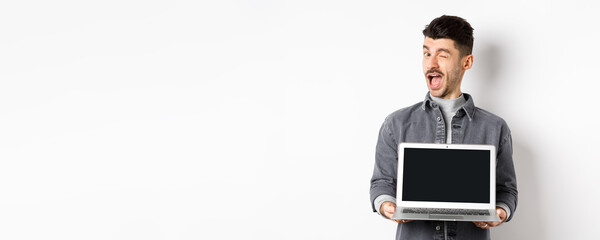Cheerful guy winking and showing empty smartphone screen, offer you advertisement, standing on...