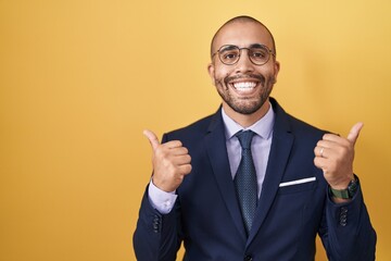 Hispanic man with beard wearing suit and tie success sign doing positive gesture with hand, thumbs up smiling and happy. cheerful expression and winner gesture.