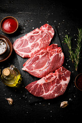 Raw pork steak on a stone board with tomato sauce, rosemary and spices. 