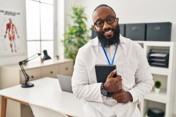 Young african american man wearing doctor uniform holding book at clinic