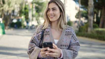 Young blonde woman smiling confident using smartphone at street