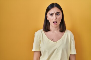 Hispanic girl wearing casual t shirt over yellow background in shock face, looking skeptical and sarcastic, surprised with open mouth