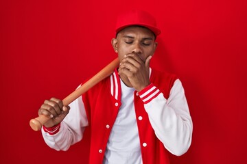 Young hispanic man playing baseball holding bat bored yawning tired covering mouth with hand....
