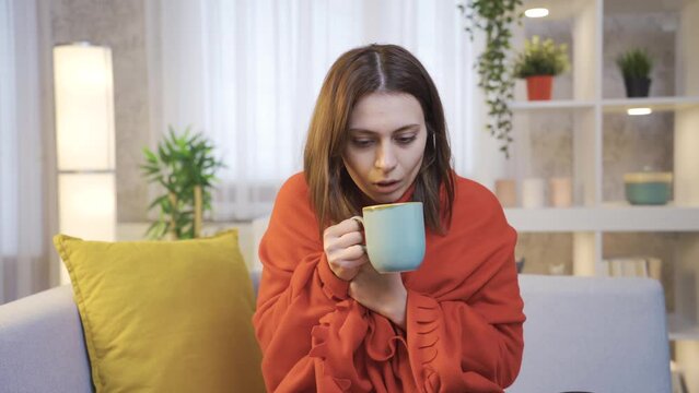 Sick Young Woman Wrapped in Pique Drinking Coffee on Sofa, Shaking From Cold.
Sick and exhausted young woman sitting on sofa in living room at home and drinking hot coffee or healthy drinks to warm up