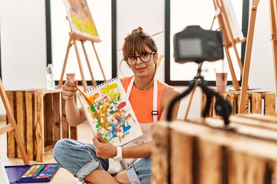 Young hispanic woman showing notebook draw to online class at art studio