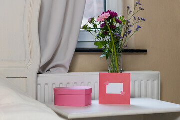 A box of chocolates, a bouquet of flowers and an envelope with a letter on the bedside table.