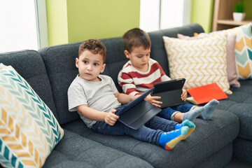 Two kids watching video on touchpad sitting on sofa at home