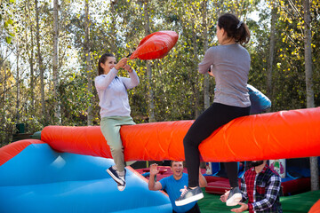 .Happy female friends fighting by big stuffed pillows sitting on log at outdoor amusement playground