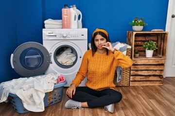 Young hispanic woman doing laundry mouth and lips shut as zip with fingers. secret and silent, taboo talking