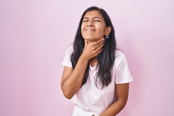Young hispanic woman standing over pink background touching painful neck, sore throat for flu, clod...