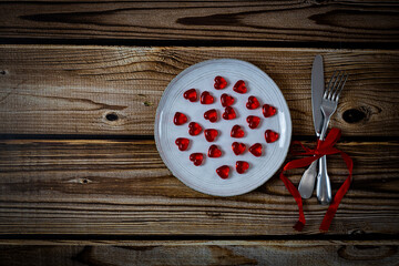 Fototapeta na wymiar Glass heart in a plate with a fork and a knife with a red ribbon on the table.
