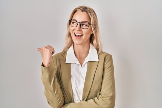 Young caucasian woman wearing glasses smiling with happy face looking and pointing to the side with thumb up.