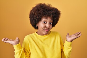 Young african american woman standing over yellow background clueless and confused expression with...