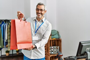 Middle age grey-haired man shop assistant holding shopping bag at clothing store