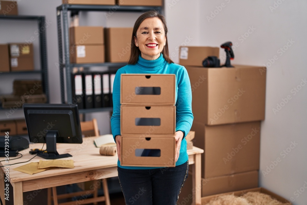 Sticker Middle age hispanic woman working at small business ecommerce holding boxes smiling with a happy and cool smile on face. showing teeth.