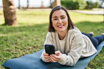 Middle age woman using smartphone lying on herb at park