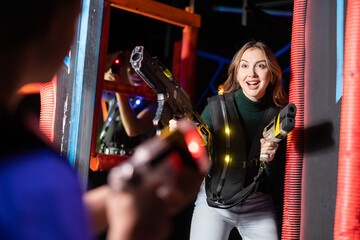 Positive girl holding laser pistol playing laser tag game with his friends