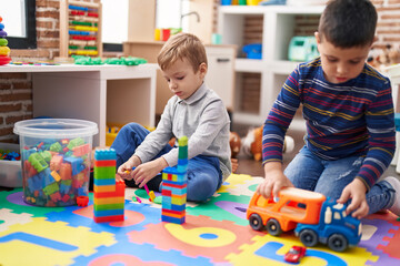 Two kids playing with construction blocks and truck toy sitting on floor at kindergarten