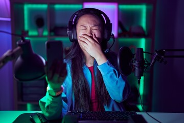 Young asian woman playing video games with smartphone bored yawning tired covering mouth with hand....