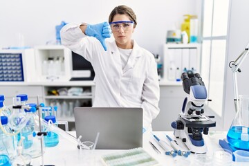 Young hispanic woman wearing scientist uniform working at laboratory with angry face, negative sign...