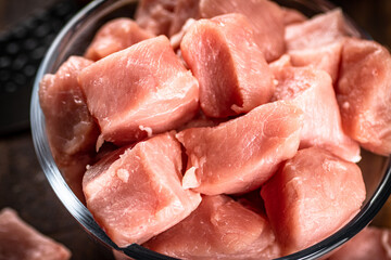 Pieces of raw pork in a bowl on a cutting board.