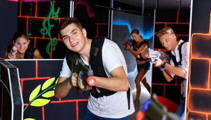 Portrait of excited happy cheerful positive glad guy with laser pistol playing laser tag in arena