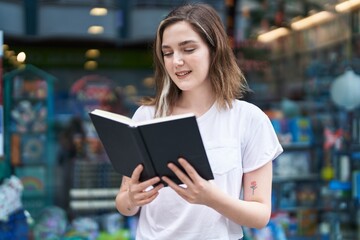 Fototapeta premium Young woman smiling confident reading book at street