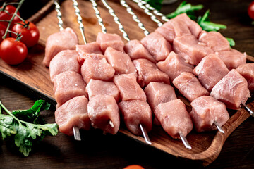 Pork kebab raw on skewers with parsley and tomatoes on a cutting board. 