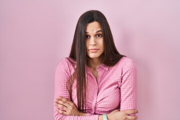 Fototapeta premium Young hispanic woman standing over pink background shaking and freezing for winter cold with sad and shock expression on face