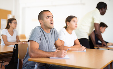 Obraz premium Caucasian man sitting at desk in classroom in university and listening carefully to lecture.