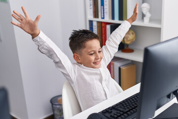 Adorable hispanic boy student using laptop with cheerful expression at classroom