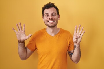 Young hispanic man standing over yellow background showing and pointing up with fingers number nine...