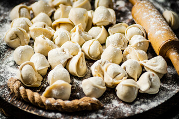 Raw homemade dumplings on tray with rolling pin. 