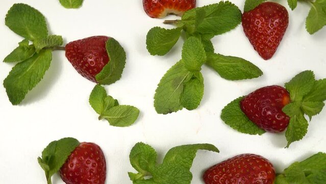 Halves of ripe strawberries and fresh mint leaves lie on a white background