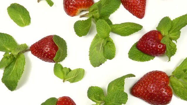 Halves of ripe strawberries and fresh mint leaves lie on a white background