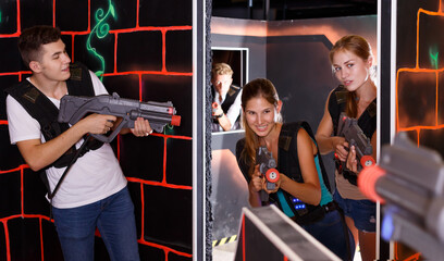 Positive players young mens and womens playing in teams in dark laser tag station