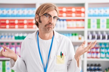 Caucasian man with mustache working at pharmacy drugstore clueless and confused expression with arms and hands raised. doubt concept.