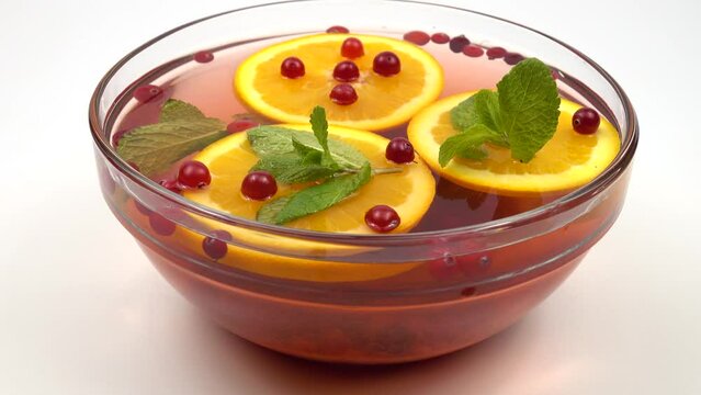 Glass bowl with non-alcoholic fruit and berry punch of cranberries, mint leaves and orange slices stands on a white table