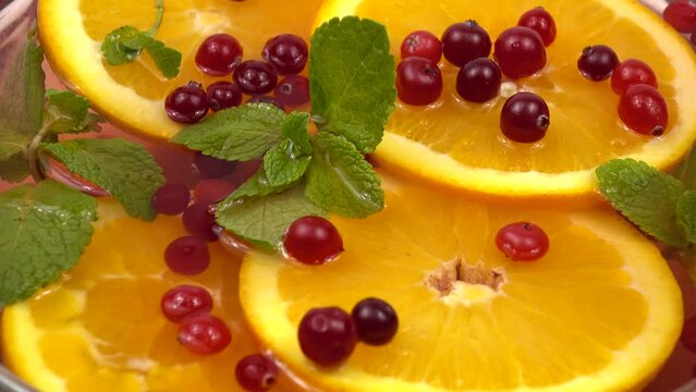 Berries of fresh cranberries fall on the slices of orange   in a glass bowl with non-alcoholic fruit and berry punch, natural background