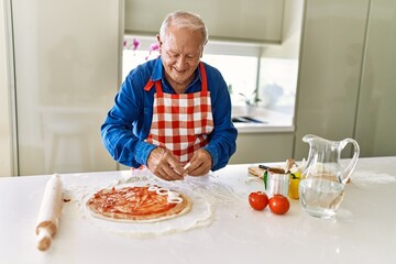 Senior man smiling confident cooking pizza at kitchen