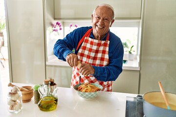 Fototapeta na wymiar Senior man smiling confident pouring pepper on spaghetti at kitchen