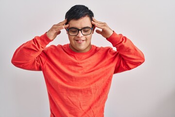 Young hispanic man with down syndrome standing over white background with hand on head, headache...