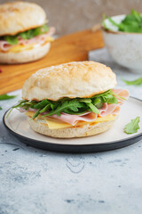 Two homemade sandwiches with ham, cheese and arugula on a concrete table.