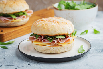 Two homemade sandwiches with ham, cheese and arugula on a concrete table.