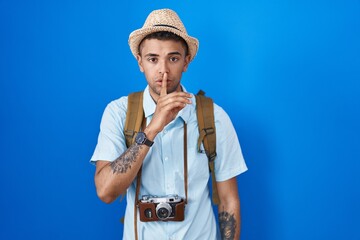 Brazilian young man holding vintage camera asking to be quiet with finger on lips. silence and secret concept.